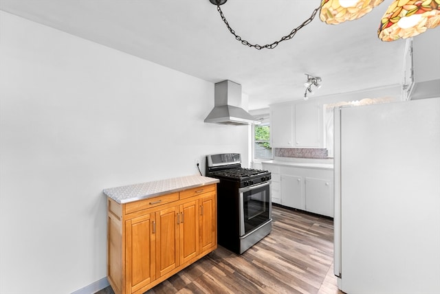 kitchen with white fridge, wall chimney exhaust hood, stainless steel gas range oven, wood-type flooring, and tasteful backsplash