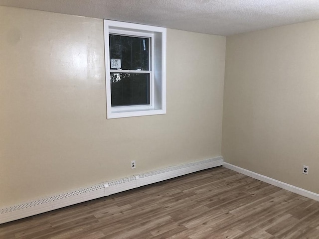 spare room with baseboard heating, hardwood / wood-style floors, and a textured ceiling