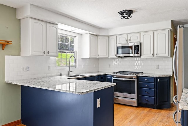 kitchen with blue cabinets, a sink, a peninsula, white cabinets, and appliances with stainless steel finishes