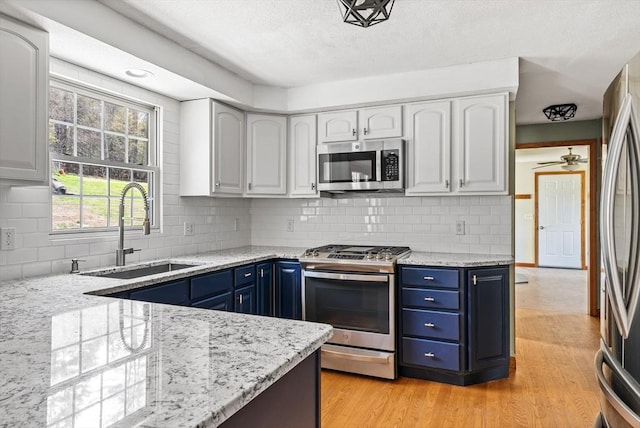 kitchen featuring appliances with stainless steel finishes, light stone countertops, blue cabinetry, and a sink