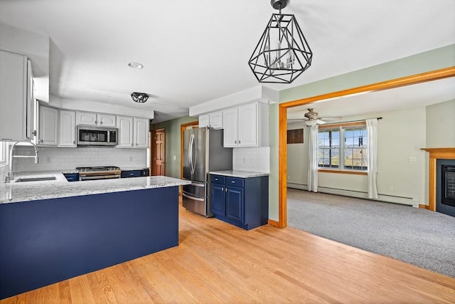 kitchen with a peninsula, a sink, stainless steel appliances, backsplash, and blue cabinetry