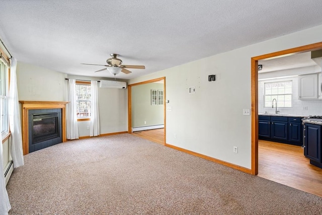 unfurnished living room featuring a ceiling fan, baseboard heating, a wall mounted air conditioner, a sink, and light colored carpet
