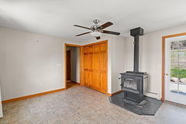 unfurnished living room with a wood stove, baseboards, a ceiling fan, and a baseboard heating unit