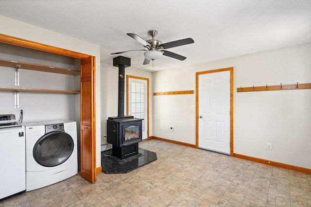 washroom featuring a ceiling fan, washing machine and dryer, baseboards, a wood stove, and laundry area