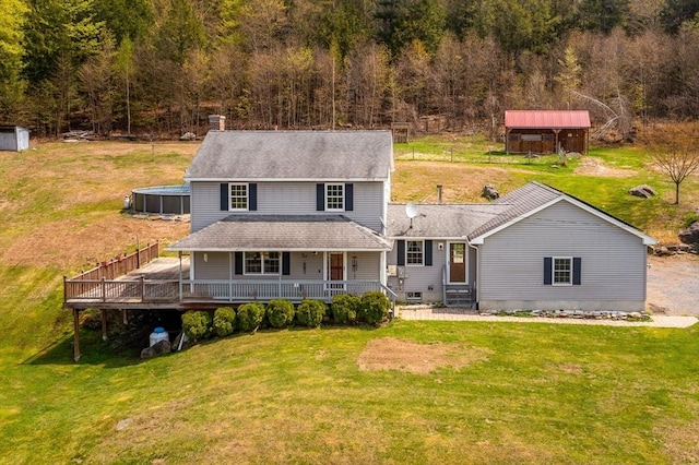 rear view of property featuring a lawn, a wooded view, a shingled roof, and covered porch