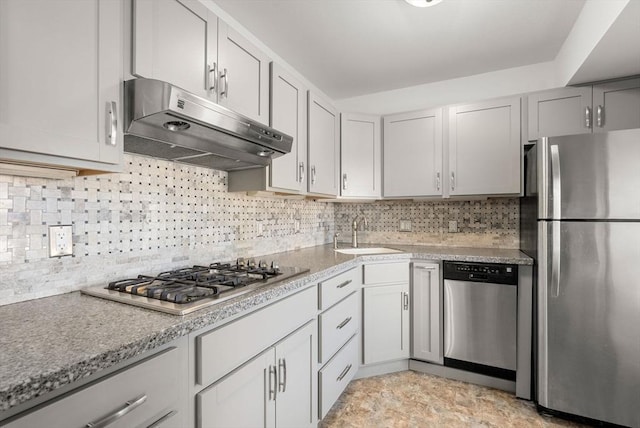 kitchen featuring a sink, stainless steel appliances, stone finish floor, under cabinet range hood, and backsplash