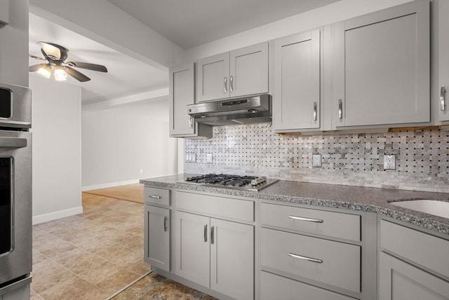 kitchen featuring baseboards, under cabinet range hood, decorative backsplash, appliances with stainless steel finishes, and stone countertops