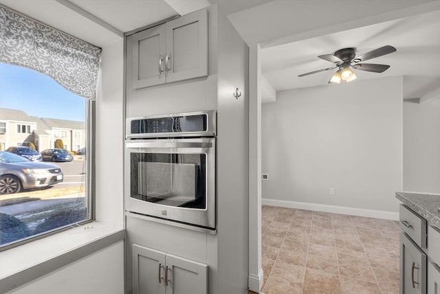 kitchen featuring ceiling fan, baseboards, gray cabinets, and oven