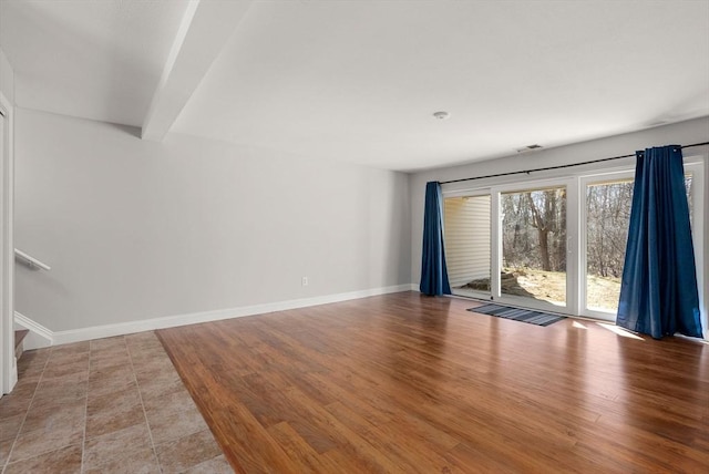 unfurnished room featuring beamed ceiling, baseboards, and wood finished floors