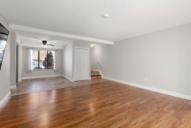 unfurnished room with stairway, baseboards, light wood-type flooring, and ceiling fan