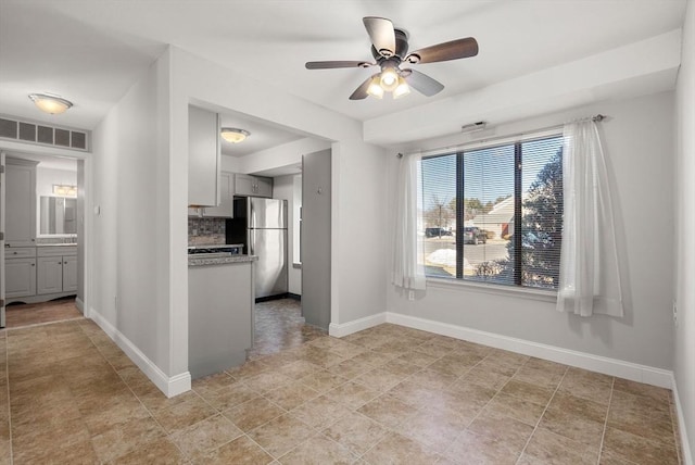 interior space with visible vents, backsplash, freestanding refrigerator, baseboards, and ceiling fan