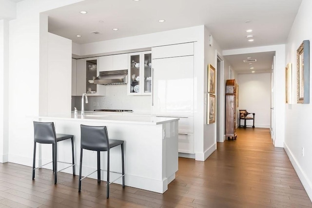 kitchen featuring a sink, wall chimney range hood, a breakfast bar area, a peninsula, and dark wood-style flooring