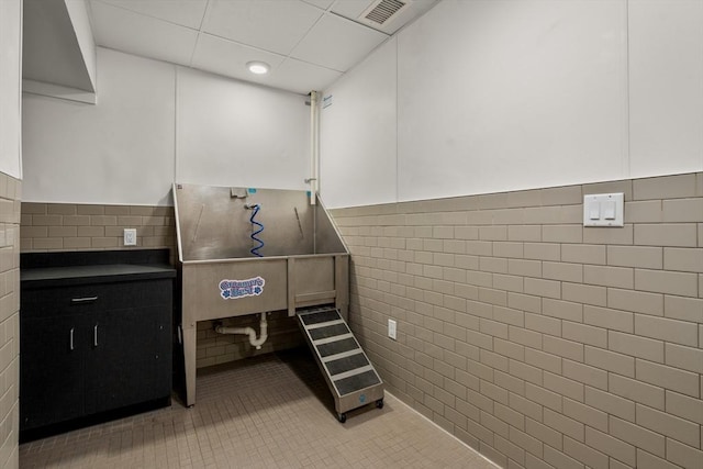 misc room with a paneled ceiling, light tile patterned floors, and tile walls