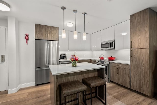 kitchen with white cabinetry, a center island, hanging light fixtures, stainless steel appliances, and light wood-type flooring