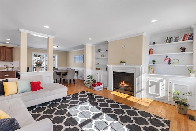 living room featuring built in shelves, recessed lighting, crown molding, and light wood-style flooring