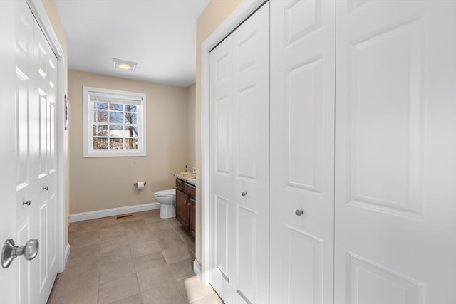 bathroom featuring tile patterned flooring, toilet, vanity, baseboards, and a closet