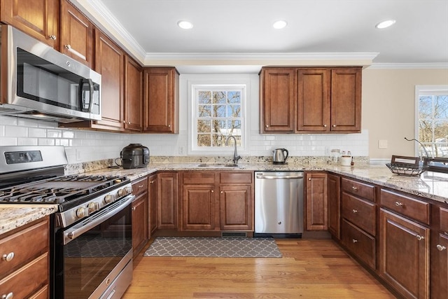 kitchen with light wood-type flooring, light stone countertops, stainless steel appliances, and a sink