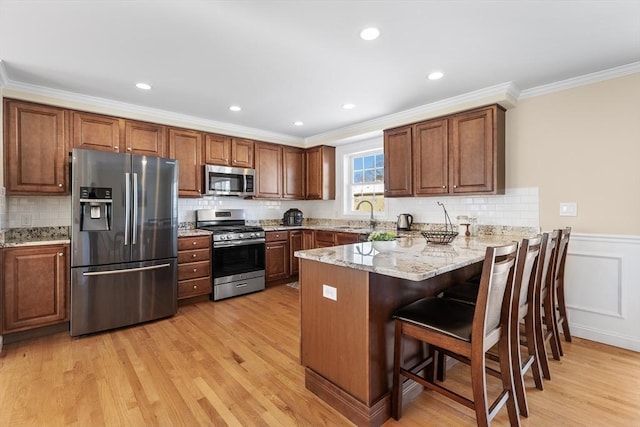 kitchen featuring a breakfast bar area, appliances with stainless steel finishes, a sink, light stone countertops, and a peninsula