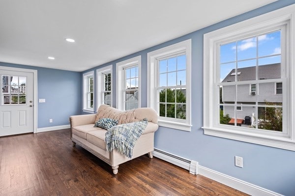 living area with baseboard heating, plenty of natural light, and dark hardwood / wood-style flooring