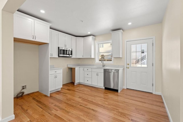 kitchen with stainless steel appliances, light wood finished floors, white cabinets, a sink, and recessed lighting