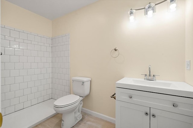 full bathroom featuring toilet, tiled shower, baseboards, and vanity