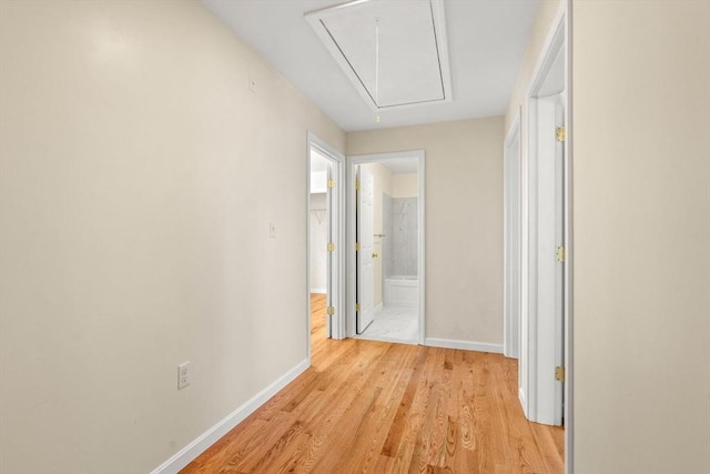 hall with attic access, light wood-type flooring, and baseboards