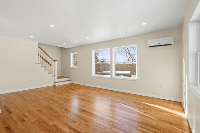 unfurnished living room featuring light wood-style floors, a wall mounted AC, stairway, baseboards, and recessed lighting