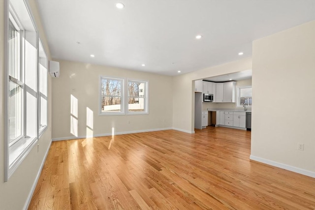 unfurnished living room featuring a wall unit AC, light wood-type flooring, baseboards, and recessed lighting