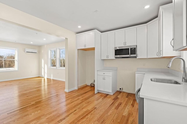 kitchen featuring stainless steel microwave, an AC wall unit, a sink, light wood-type flooring, and white cabinetry