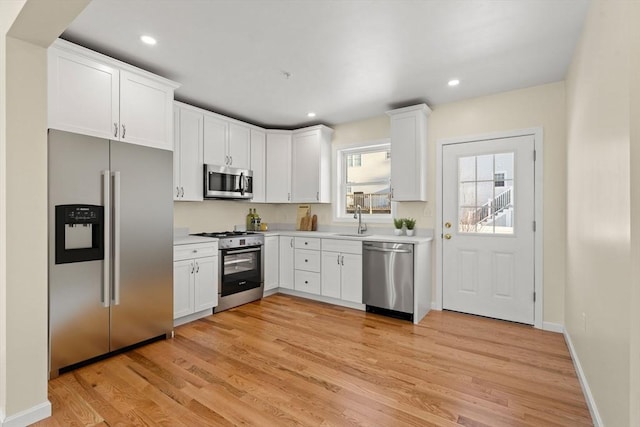 kitchen featuring stainless steel appliances, light countertops, white cabinetry, light wood-style floors, and a sink