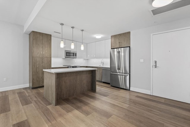 kitchen featuring white cabinets, appliances with stainless steel finishes, a kitchen island, sink, and hanging light fixtures