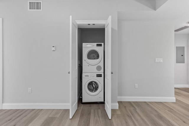 laundry room with stacked washer / drying machine, electric panel, and light wood-type flooring