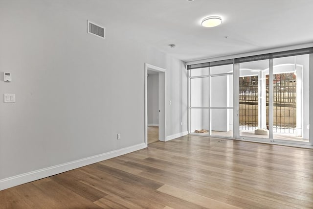 spare room with floor to ceiling windows and light hardwood / wood-style flooring