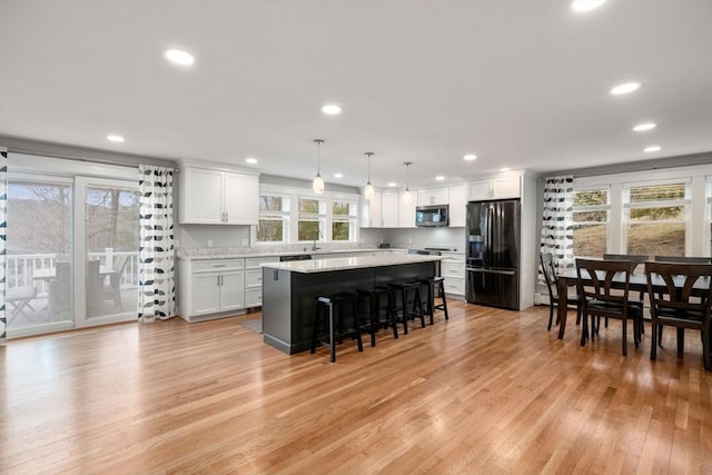 kitchen featuring light wood-style flooring, a kitchen island, stainless steel microwave, a breakfast bar, and black refrigerator with ice dispenser