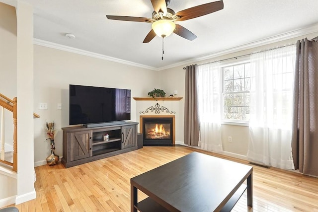 living area with stairway, ornamental molding, a ceiling fan, and light wood finished floors