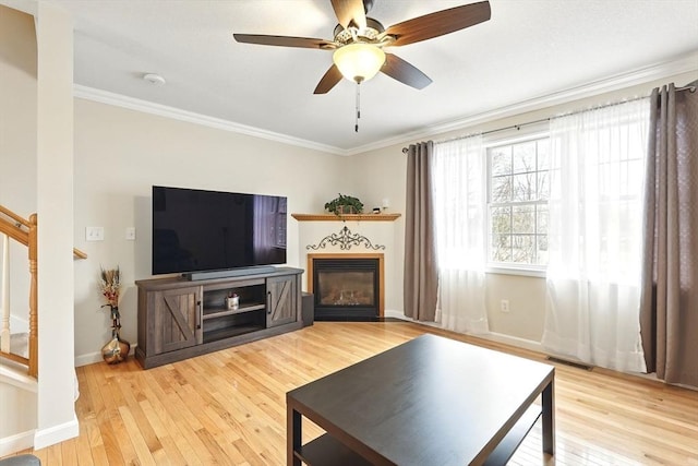 living room featuring crown molding, ceiling fan, stairway, and light wood-type flooring