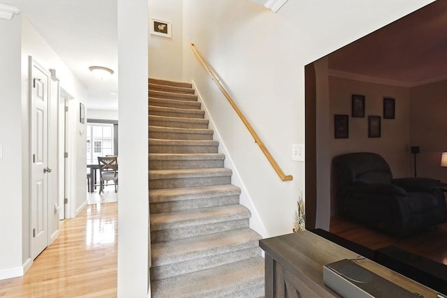 stairway featuring baseboards, ornamental molding, and wood finished floors