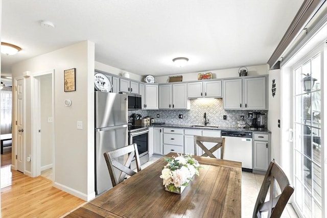 kitchen with baseboards, gray cabinets, tasteful backsplash, a sink, and appliances with stainless steel finishes