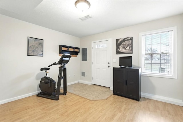 workout room featuring visible vents, baseboards, light wood finished floors, and electric panel