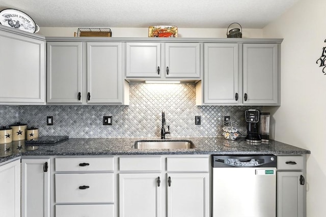 kitchen with stainless steel dishwasher, decorative backsplash, dark stone counters, gray cabinets, and a sink