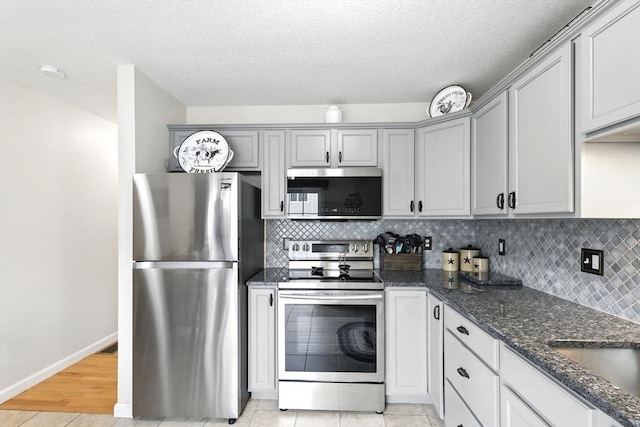 kitchen with gray cabinets, backsplash, appliances with stainless steel finishes, a sink, and dark stone counters