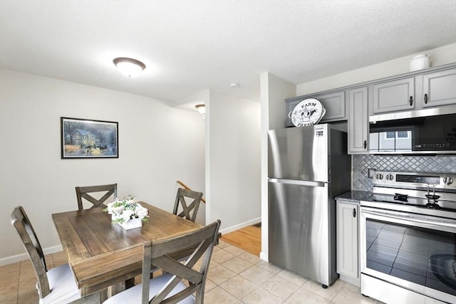 kitchen featuring light tile patterned flooring, appliances with stainless steel finishes, baseboards, backsplash, and gray cabinetry