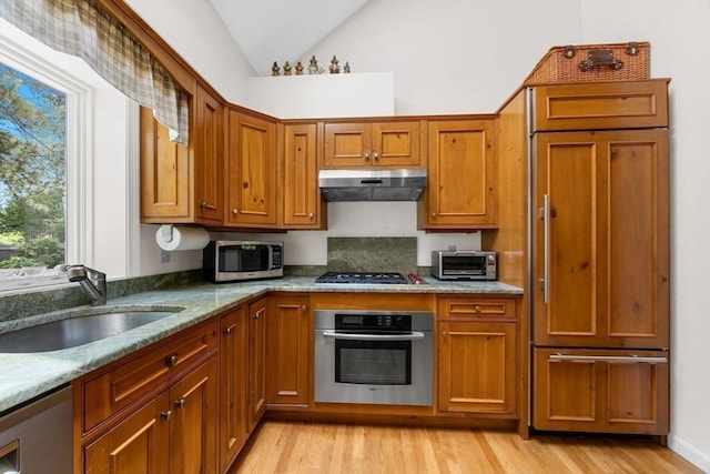21 Gramps Way, Chatham, MA 02659 - kitchen featuring appliances with stainless steel finishes, under cabinet range hood, vaulted ceiling, brown cabinets, and light wood finished floors