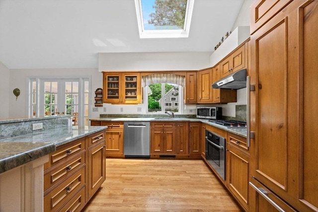 21 Gramps Way, Chatham, MA 02659 - kitchen with stainless steel appliances, a skylight, under cabinet range hood, brown cabinets, and light wood-style flooring