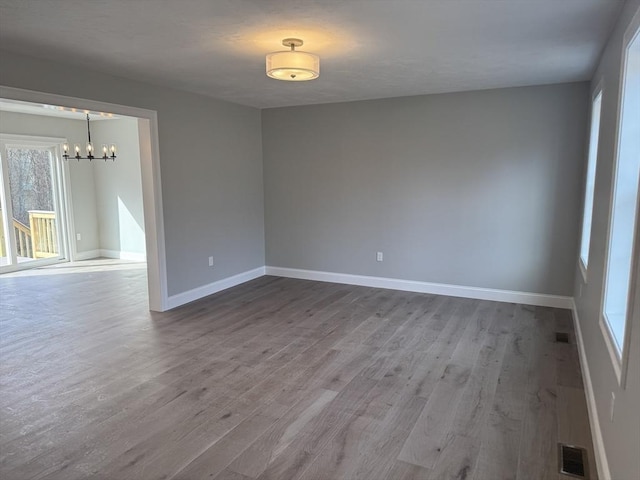 spare room featuring a chandelier, wood finished floors, visible vents, and baseboards