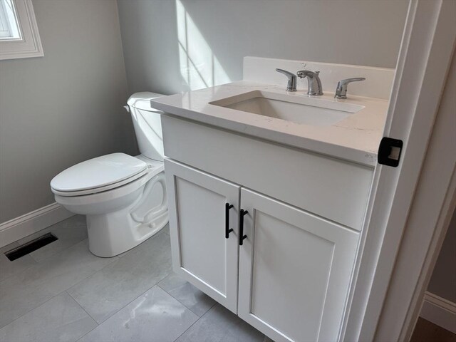 half bathroom with baseboards, visible vents, vanity, and toilet