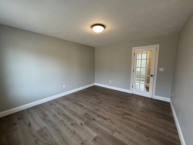 spare room with a textured ceiling, dark wood-type flooring, and baseboards