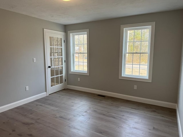 unfurnished room with baseboards, a textured ceiling, wood finished floors, and a healthy amount of sunlight