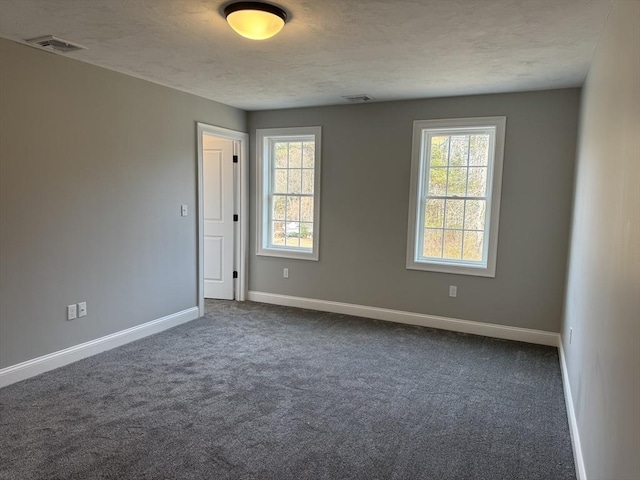 empty room with baseboards, visible vents, dark carpet, and a wealth of natural light