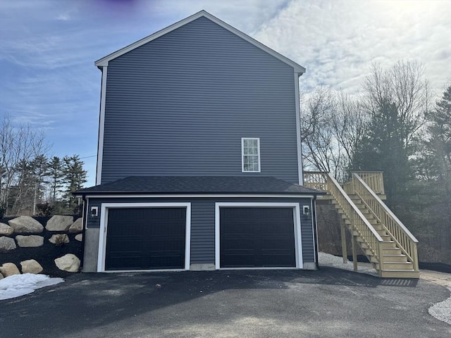 view of home's exterior with stairs, driveway, roof with shingles, and a garage